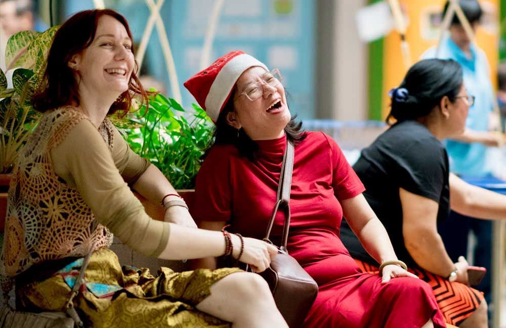 Two women are sitting on a bench and one is wearing a santa hat.