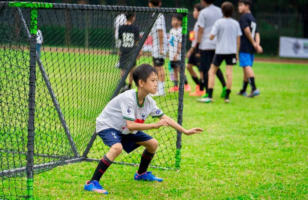 A young boy is squatting in front of a soccer goal.
