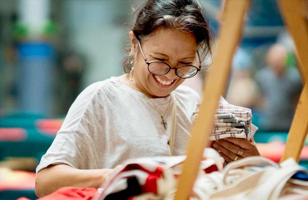 A woman wearing glasses is smiling while looking at a piece of fabric.