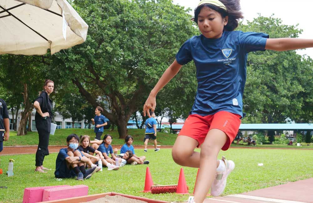 A young girl is jumping in the air while a group of people watch.