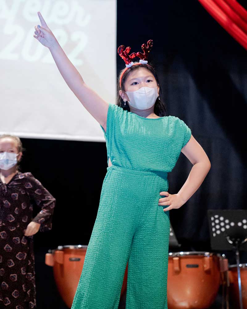 A girl wearing a green jumpsuit and a reindeer headband is pointing up.