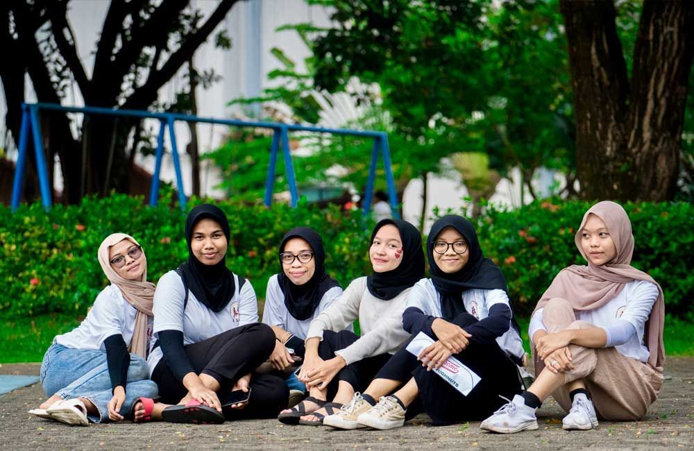 A group of young women are sitting on the ground in a park.