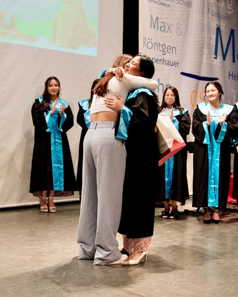A woman in a graduation gown is hugging another woman