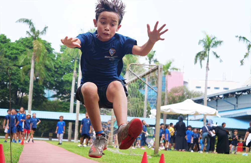A young boy is jumping over cones on a track.