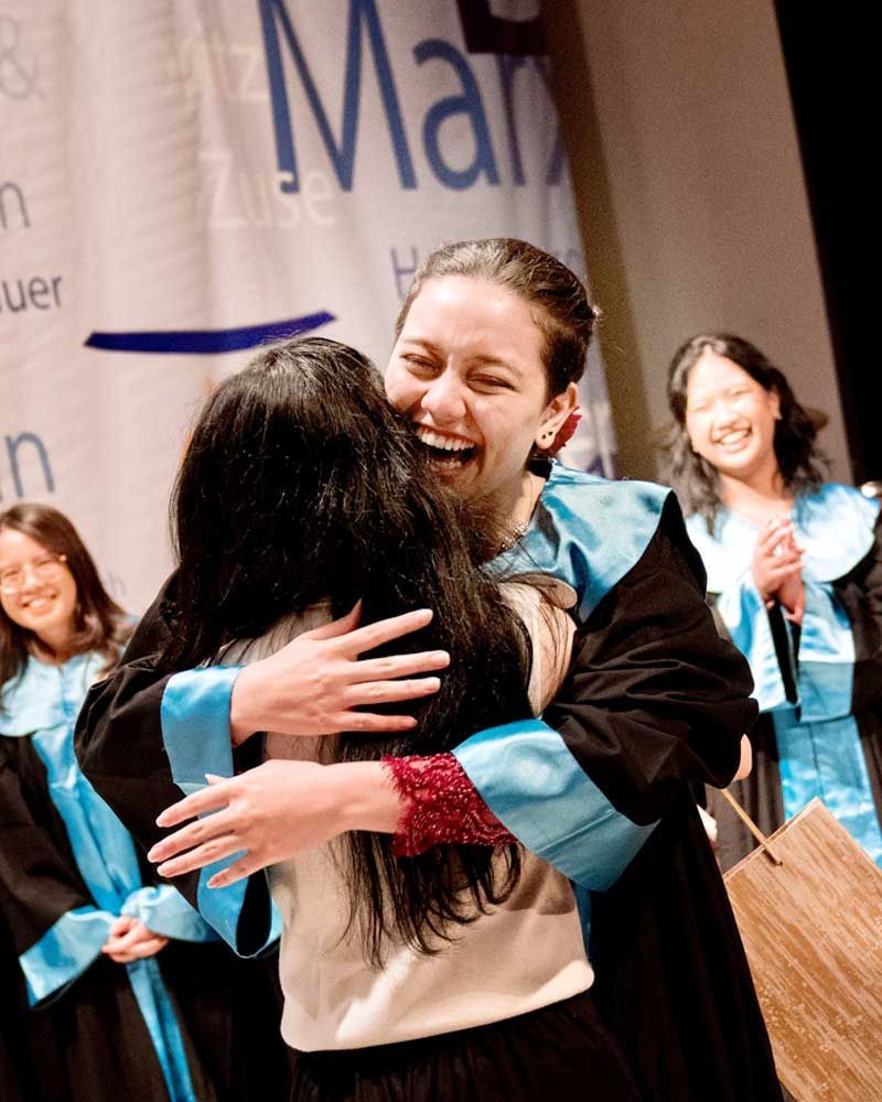 A woman in a graduation cap and gown is hugging another woman