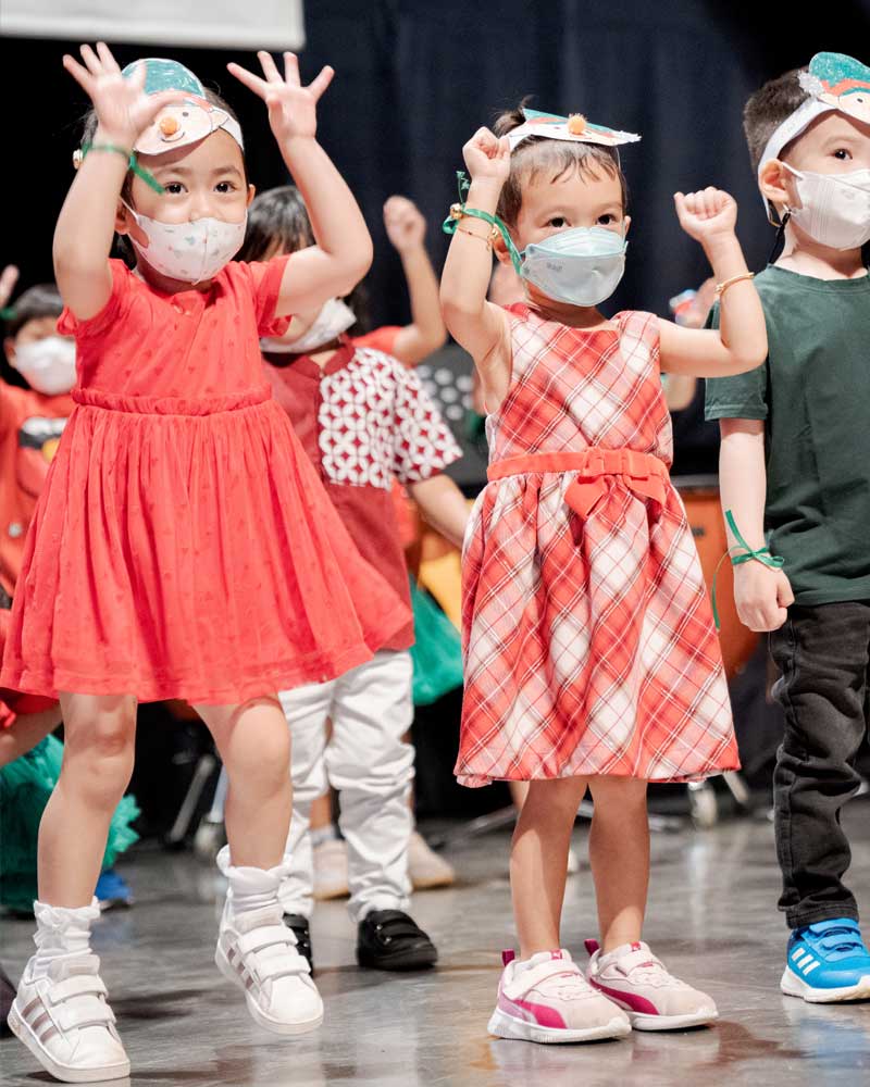 A group of children wearing face masks are dancing on a stage.