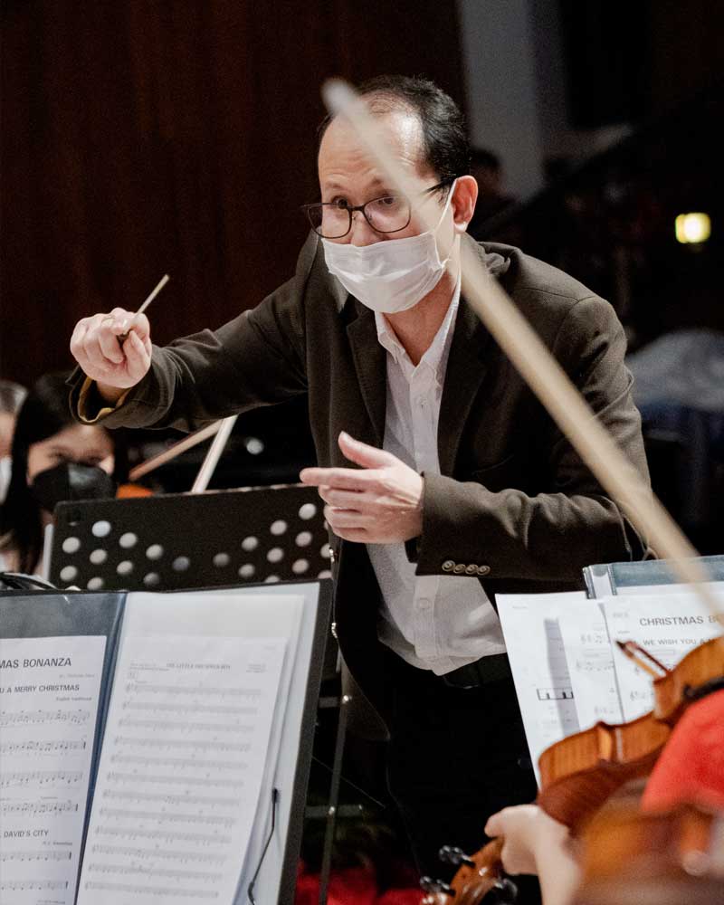 A man wearing a mask is leading an orchestra