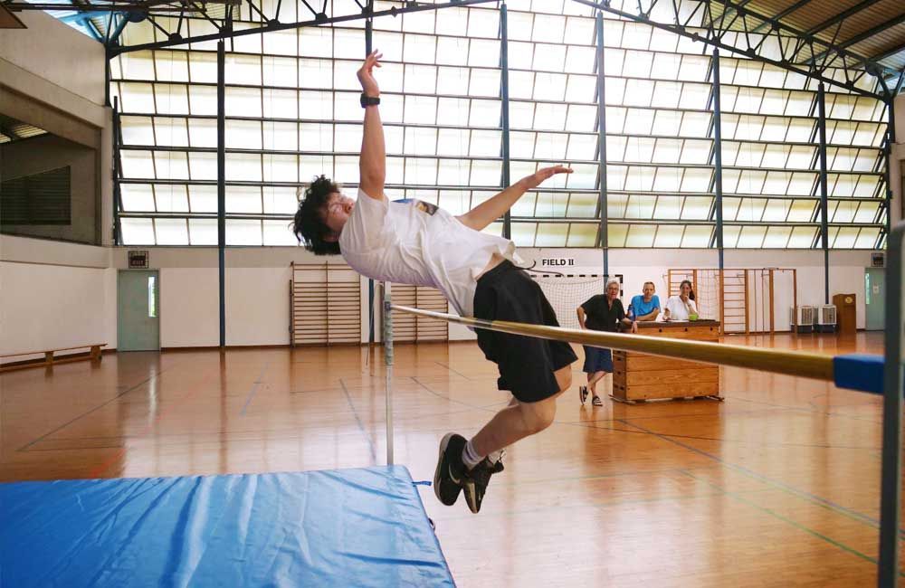 A man is jumping over a pole in a gym.