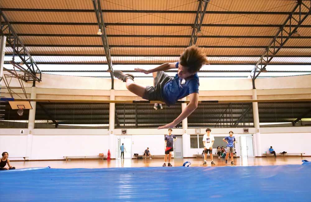 A young boy is doing a trick on a trampoline in a gym.