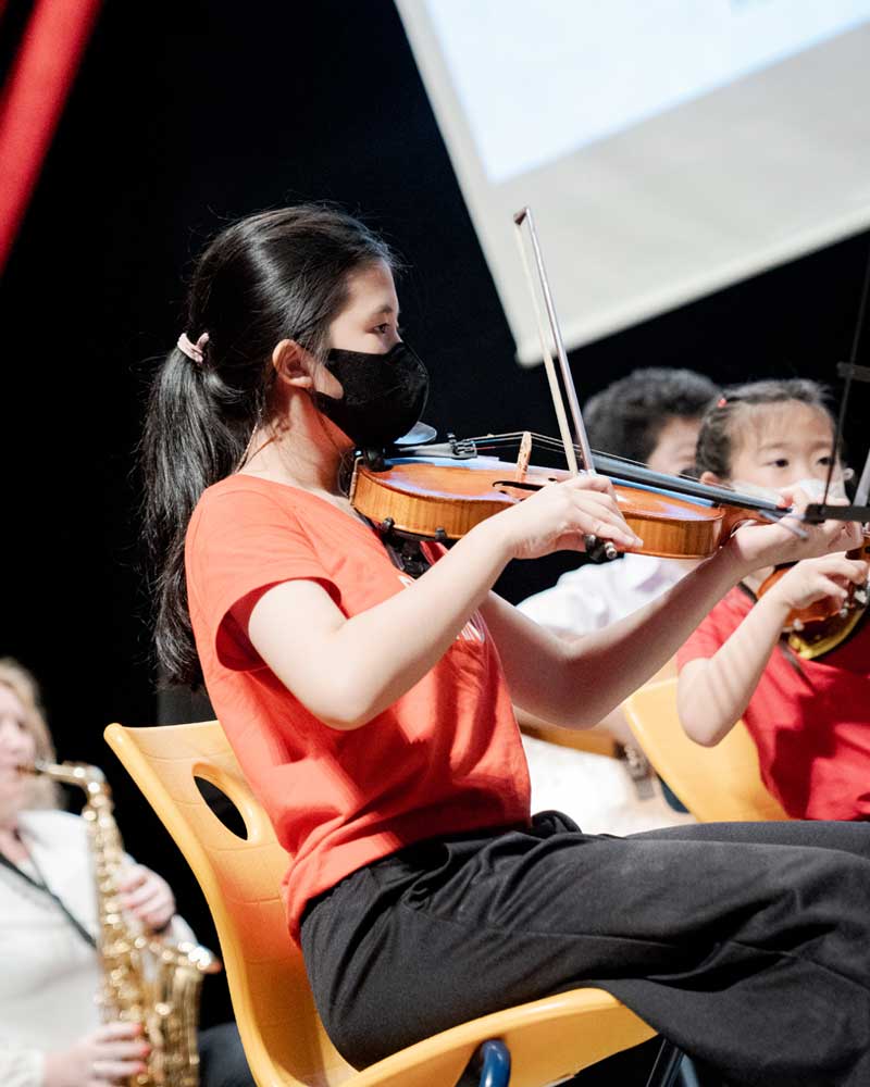A woman wearing a mask is playing a violin in an orchestra
