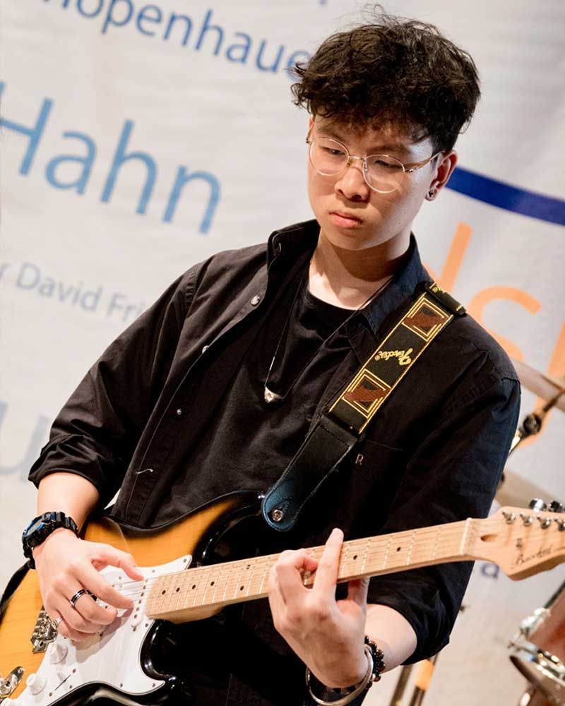 A man is playing a guitar in front of a sign that says hahn