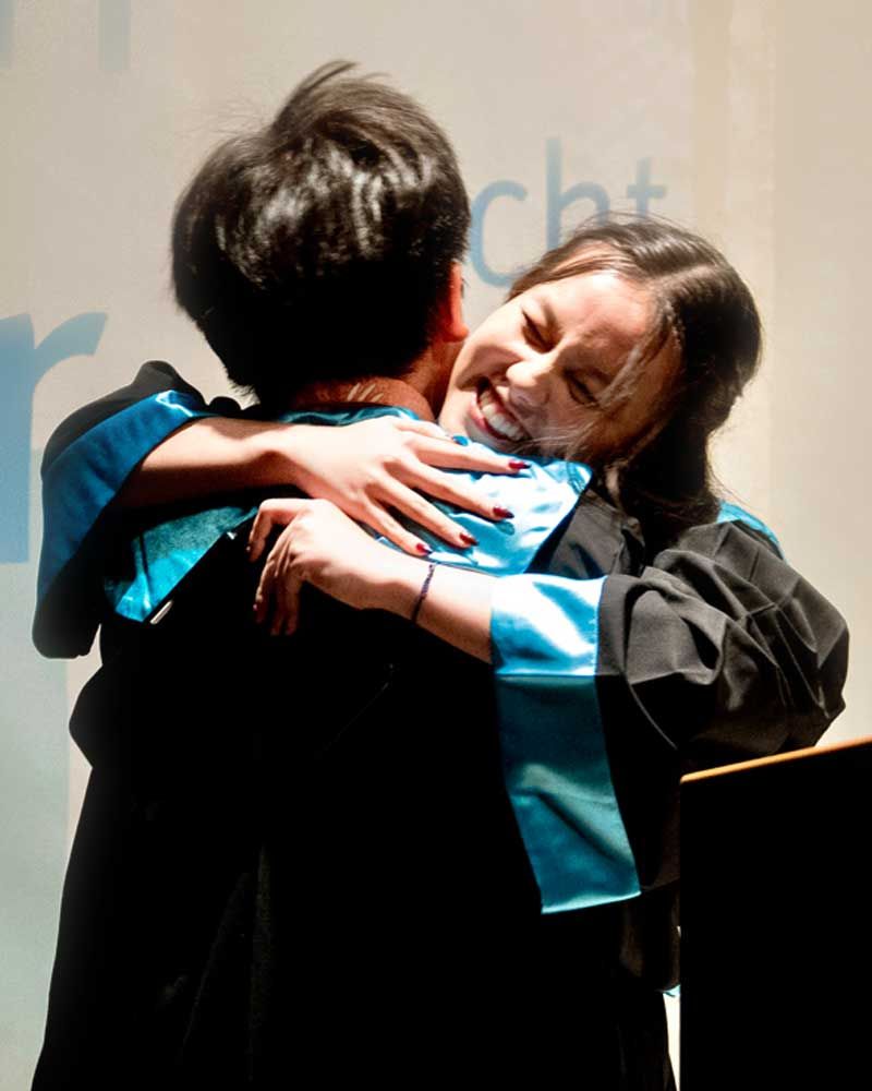 A woman in a graduation gown is hugging a man