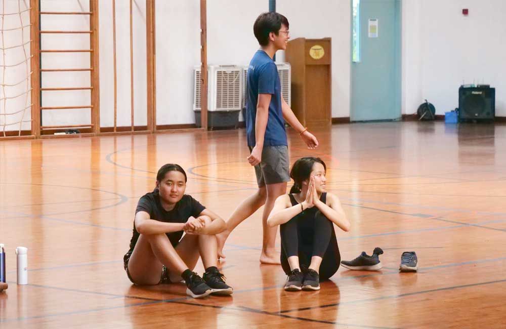 A group of people are sitting on the floor in a gym.