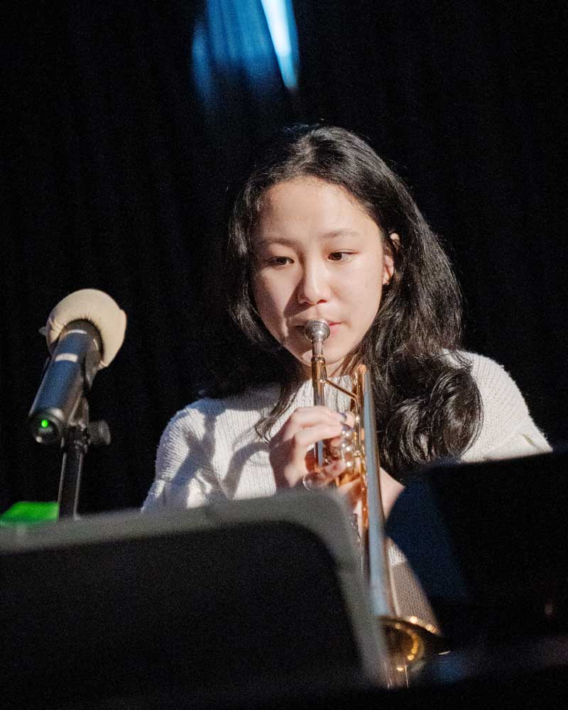A young woman is playing a trumpet in front of a microphone.