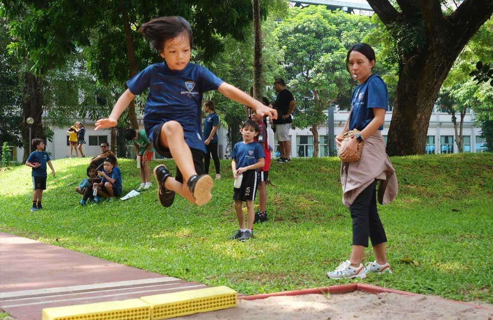 A young girl is jumping in the air while a woman watches.