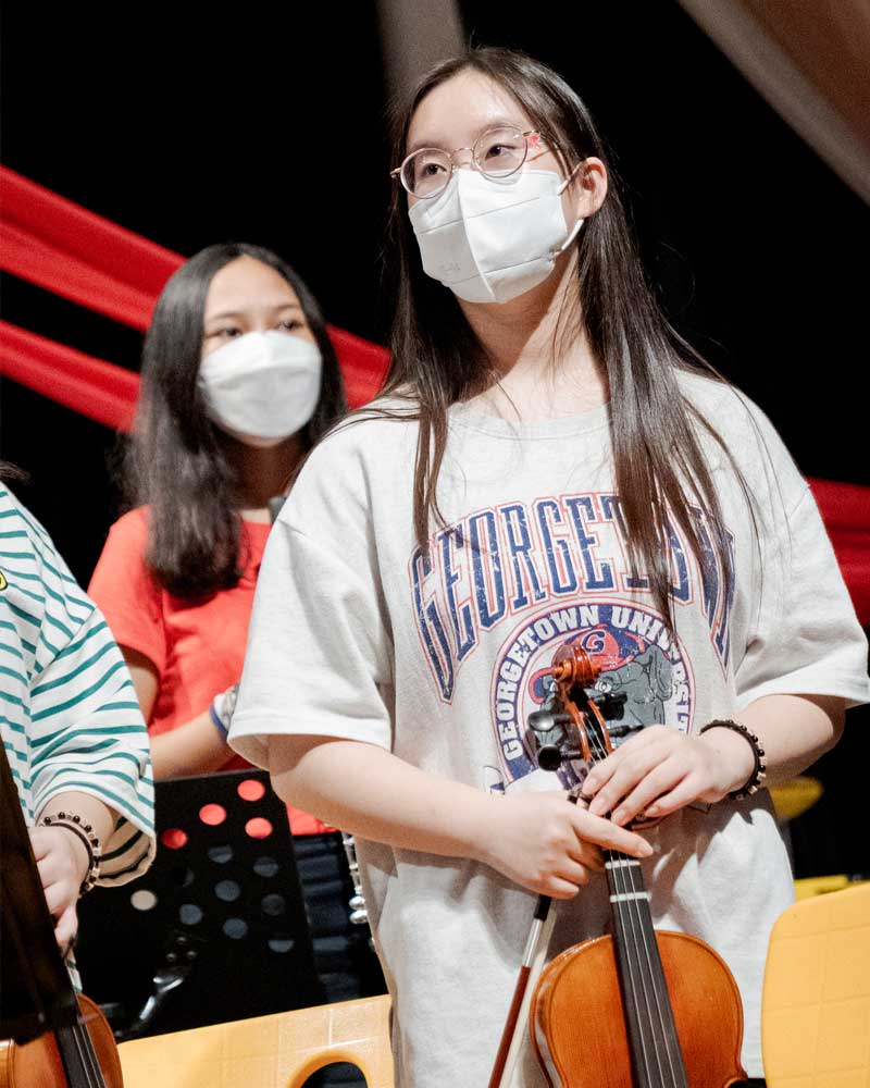 A girl wearing a mask is holding a violin.