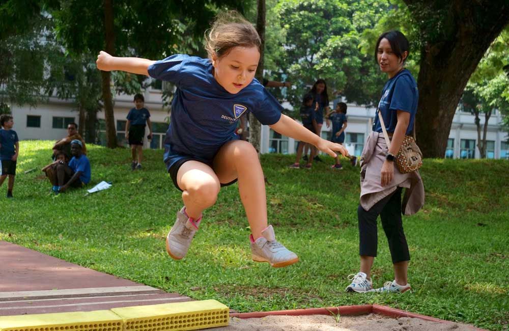 A young girl is jumping in the air while a woman watches.