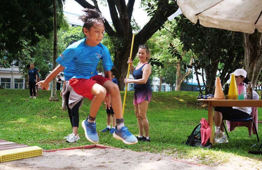 A young boy is jumping in the air while holding a pole.