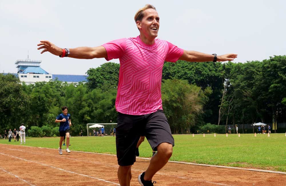 A man in a pink shirt is running on a track with his arms outstretched.