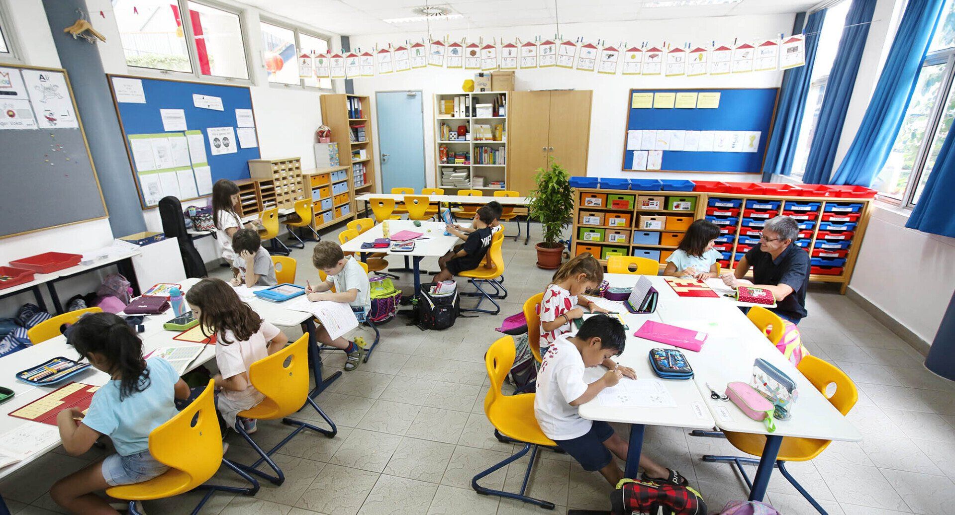 A group of children are sitting at tables in a classroom.