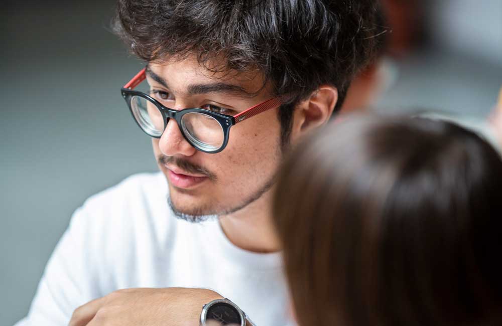 A man wearing glasses is talking to a woman.
