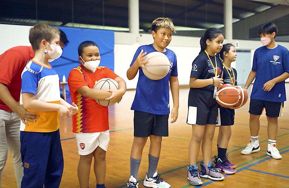 A group of children are standing in a gym holding basketballs.