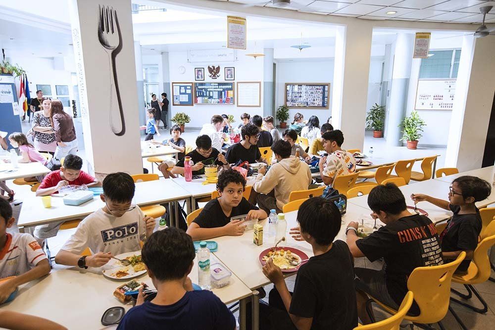 A group of children are sitting at tables in a cafeteria eating food.
