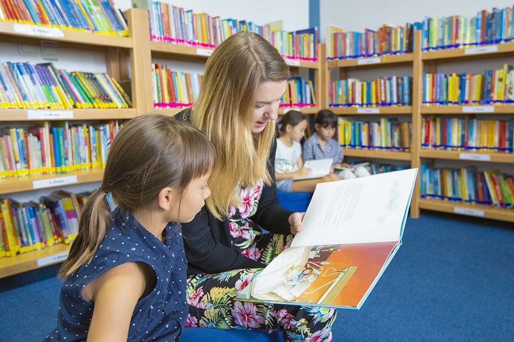 A woman is reading a book to a little girl in a library.