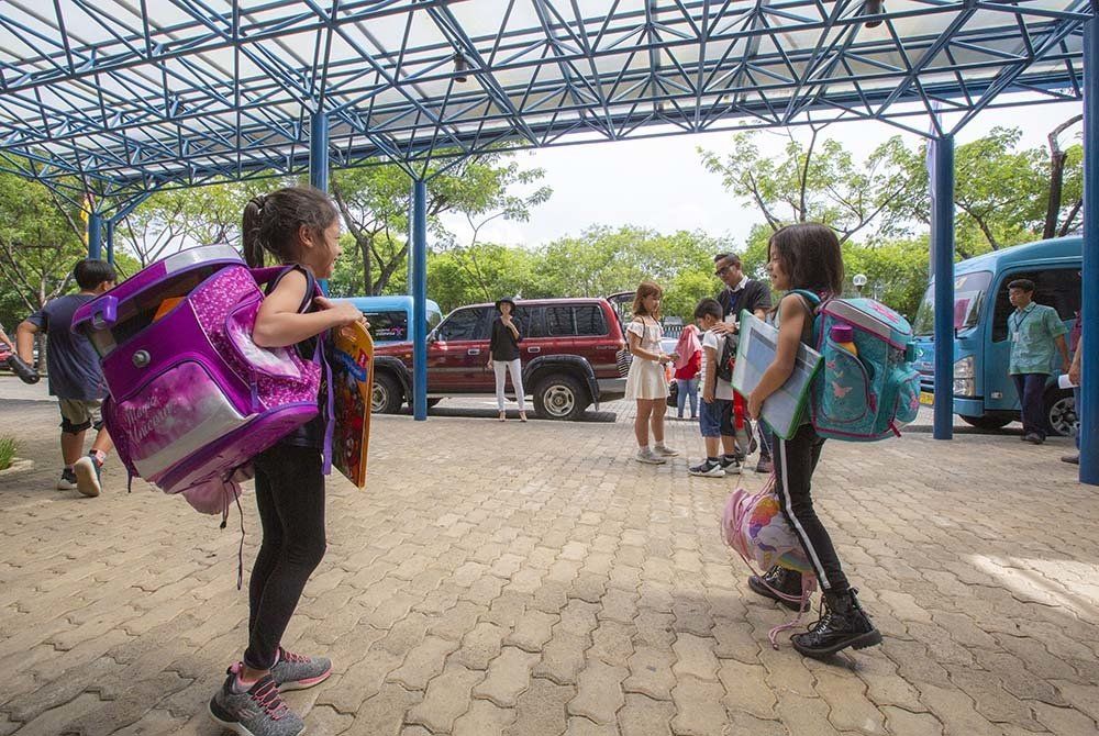 A group of children with backpacks are standing under a canopy.