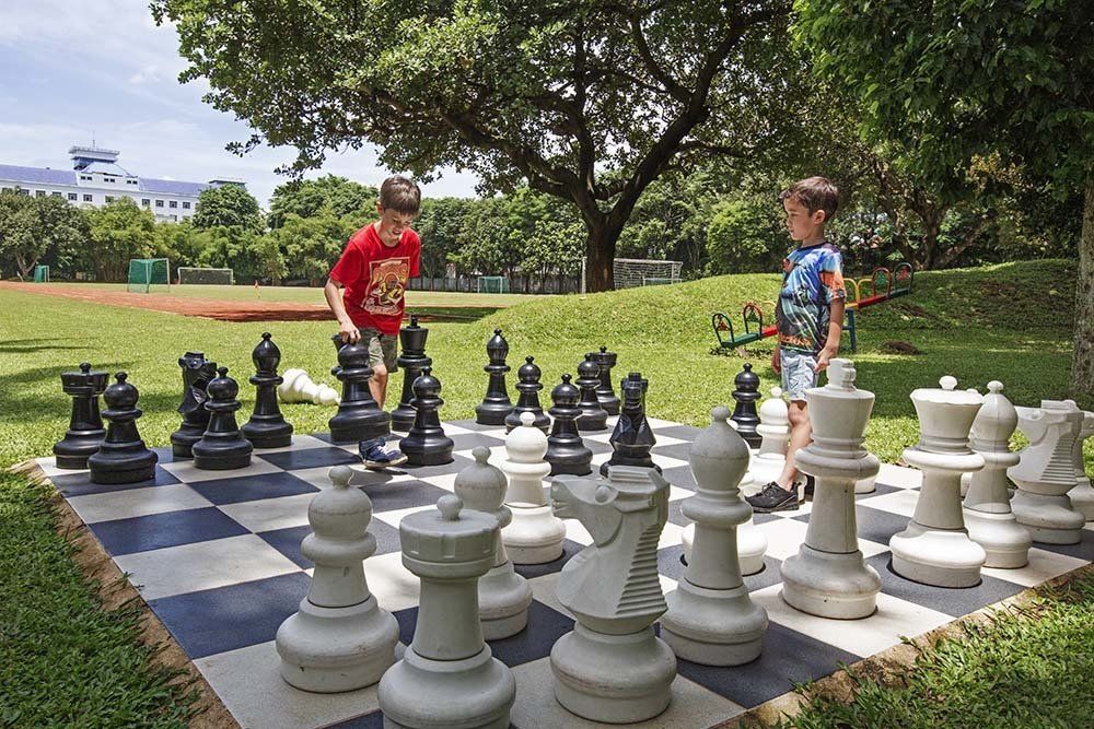 Two young boys are playing a game of chess on a giant chess board in a park.
