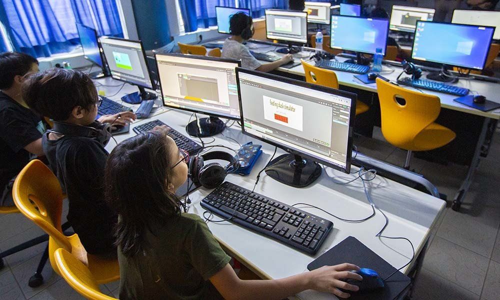 A group of people are sitting at desks in front of computer monitors.