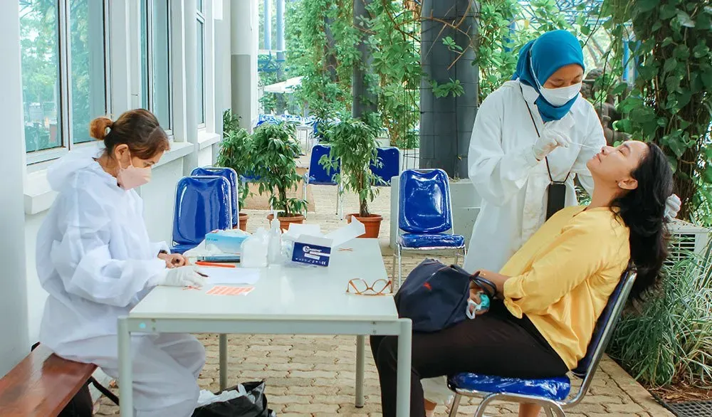 A woman is sitting at a table while a doctor takes a swab from her nose.
