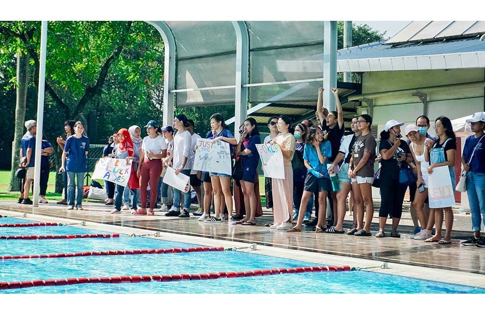 A group of people are standing around a swimming pool holding signs.