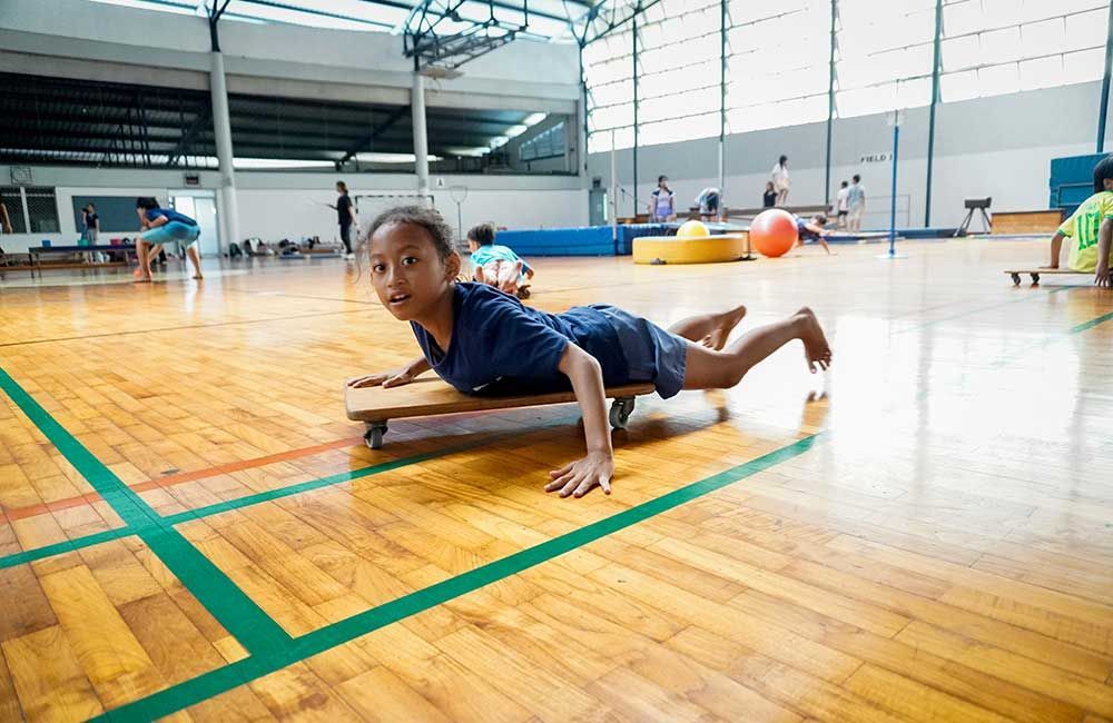 A young girl is crawling on a wooden board in a gym.