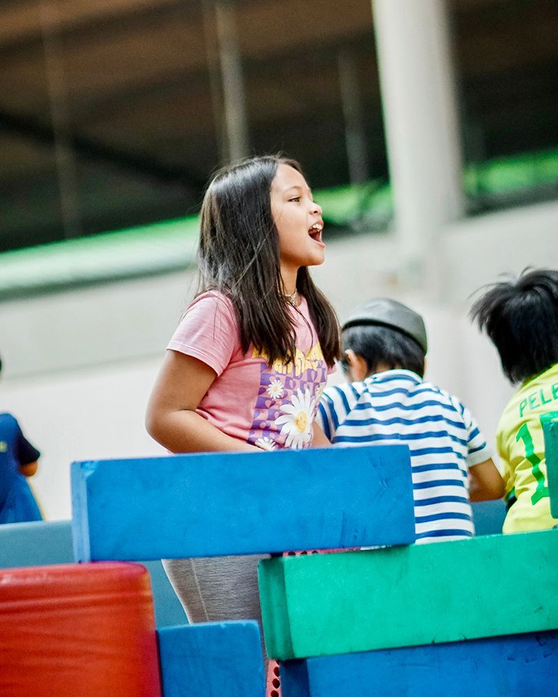 A little girl is sitting on a bench with other children.