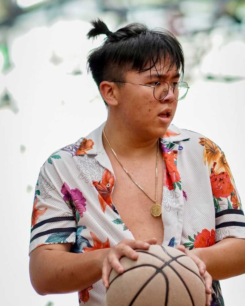 A young man wearing glasses and a floral shirt is holding a basketball.