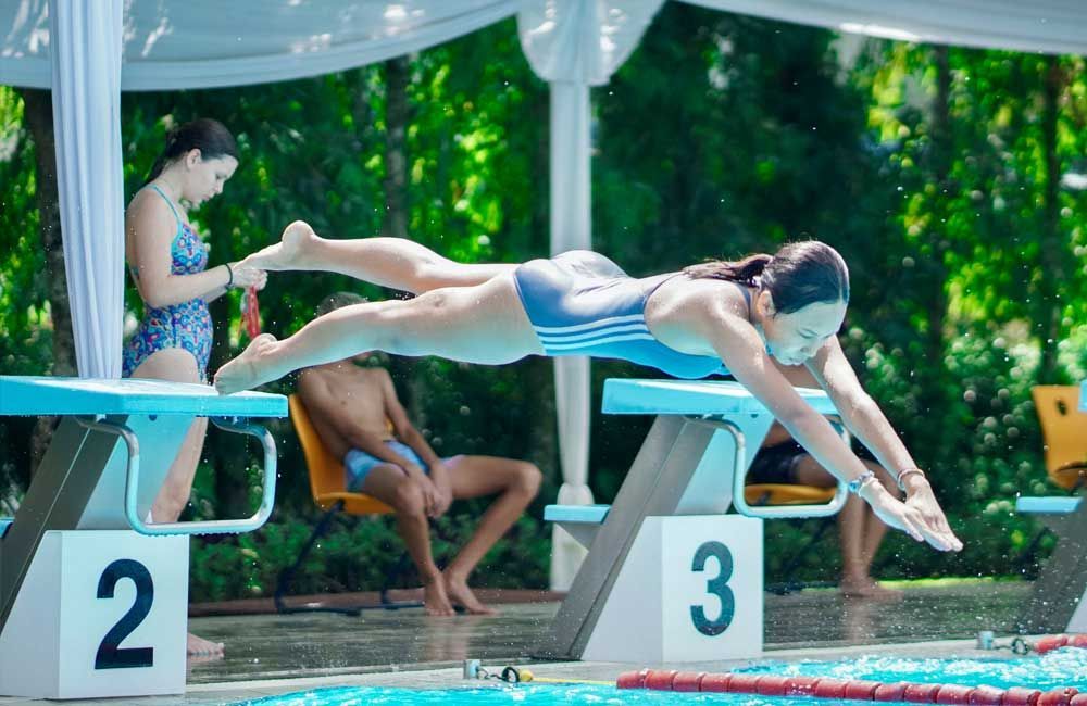 A woman is diving into a swimming pool with a mask on her face.