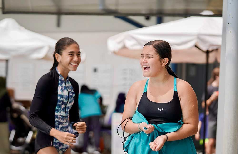 Two young girls are standing next to each other in front of a pool.