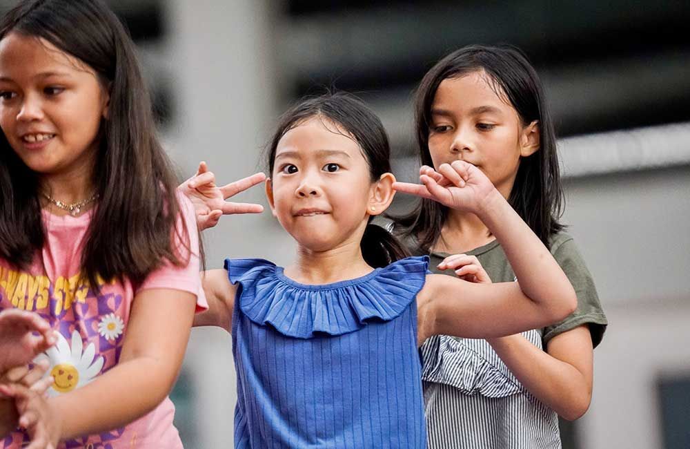 Three young girls are standing next to each other making peace signs.