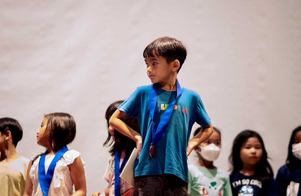A boy wearing a medal is standing in front of a group of children.
