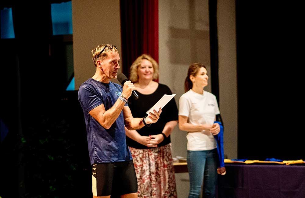A man is speaking into a microphone while two women stand behind him.