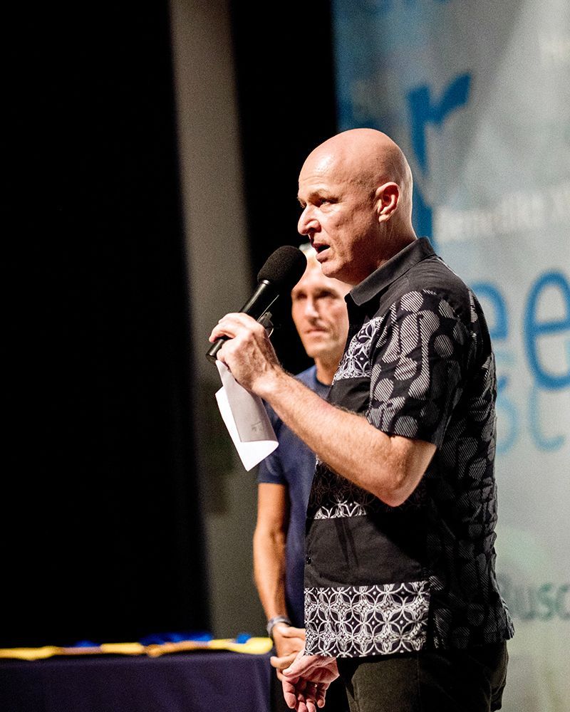 A bald man is speaking into a microphone on a stage