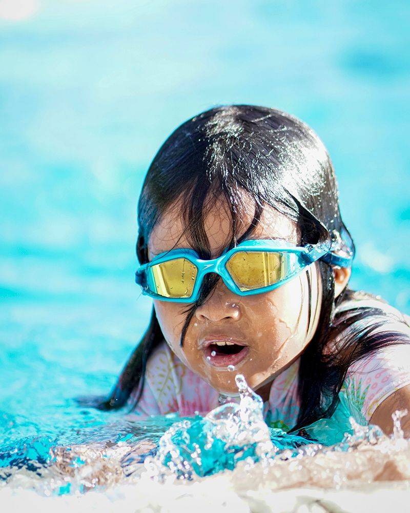 A little girl wearing goggles is swimming in a pool.