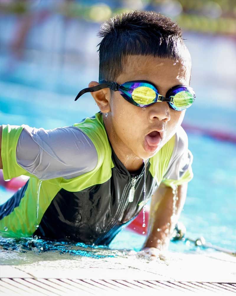 A young boy wearing goggles is swimming in a pool.