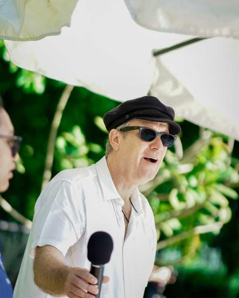 A man wearing sunglasses and a hat is holding a microphone