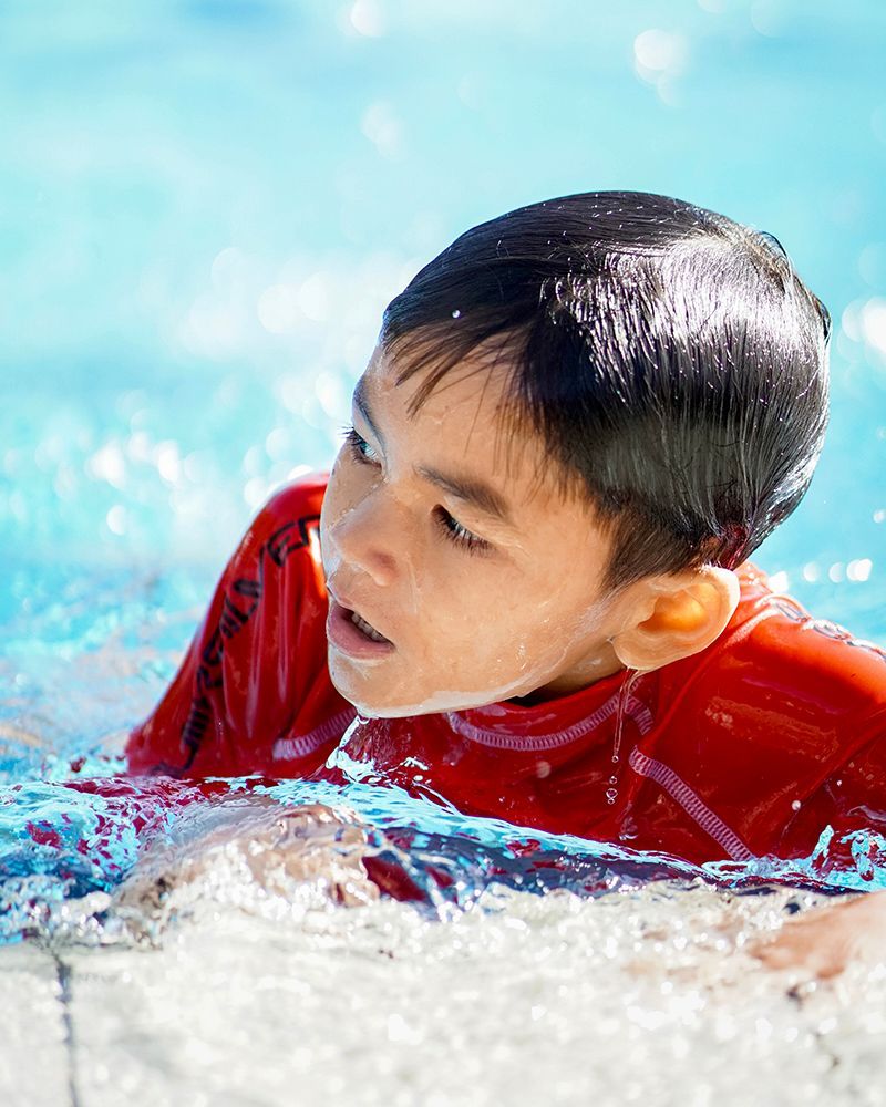 A young boy in a red shirt is swimming in a pool.