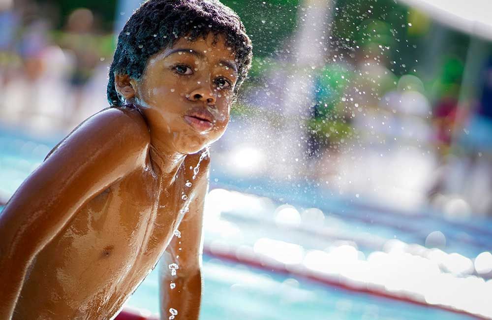 Young boy emerging from a swimming pool, with water droplets on his face