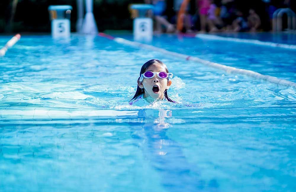 A young girl wearing goggles is swimming in a swimming pool.