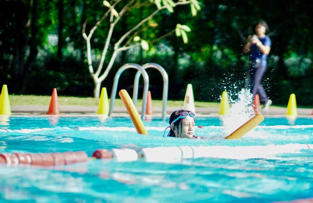 A young girl is swimming in a swimming pool with foam noodles.