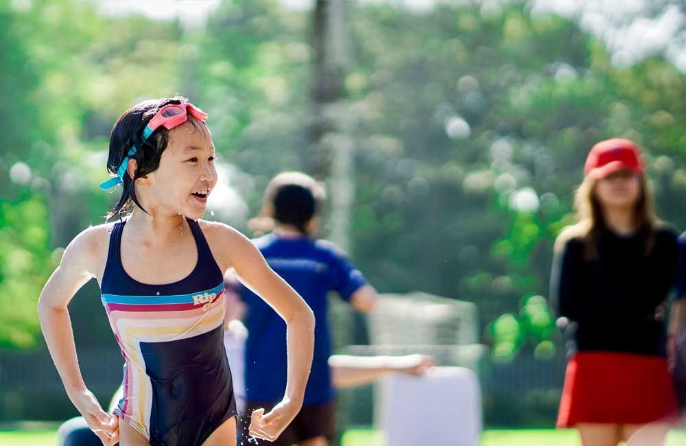 A young girl in a swimsuit and goggles is running on a field.